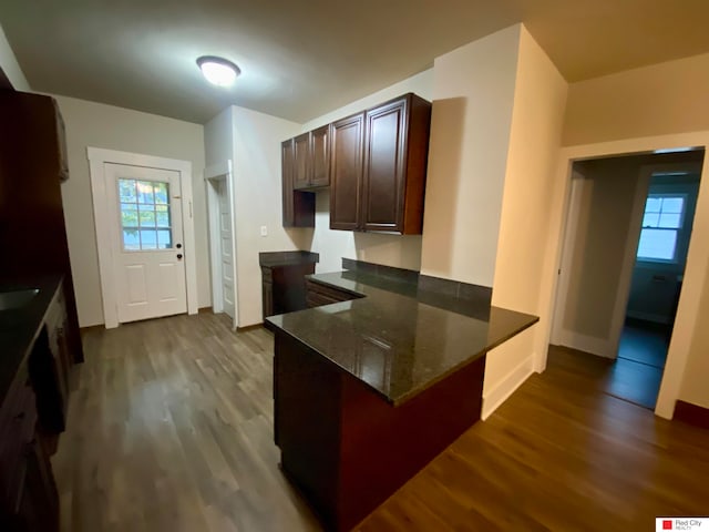 kitchen with kitchen peninsula, dark brown cabinetry, hardwood / wood-style flooring, and dark stone counters