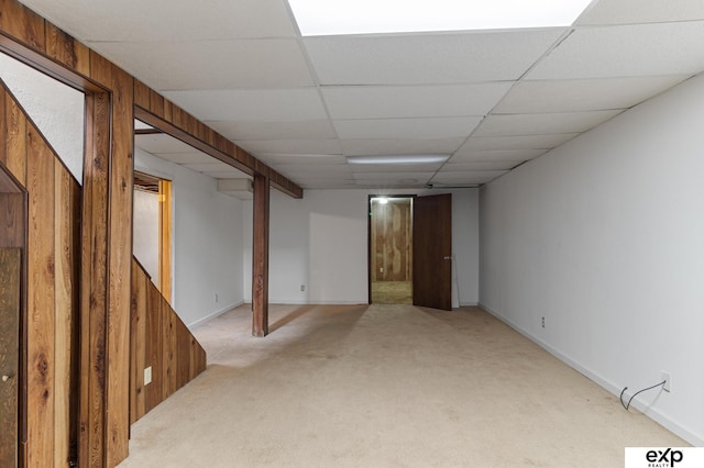 basement with a paneled ceiling, wooden walls, and light colored carpet