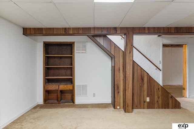 basement featuring light carpet and wood walls