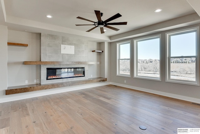 unfurnished living room with a tile fireplace, ceiling fan, and light hardwood / wood-style floors