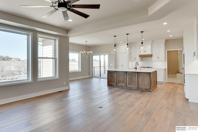 kitchen featuring hanging light fixtures, a kitchen island with sink, white cabinets, and light wood-type flooring