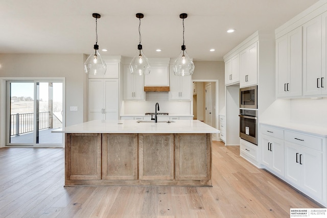 kitchen featuring white cabinetry, a kitchen island with sink, built in microwave, decorative light fixtures, and oven