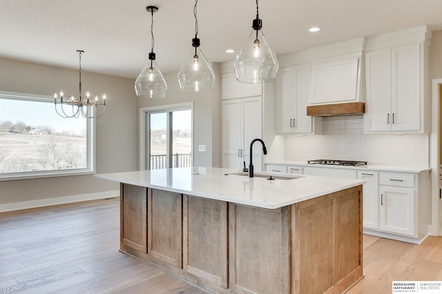 kitchen with white cabinetry, decorative light fixtures, sink, and a large island with sink