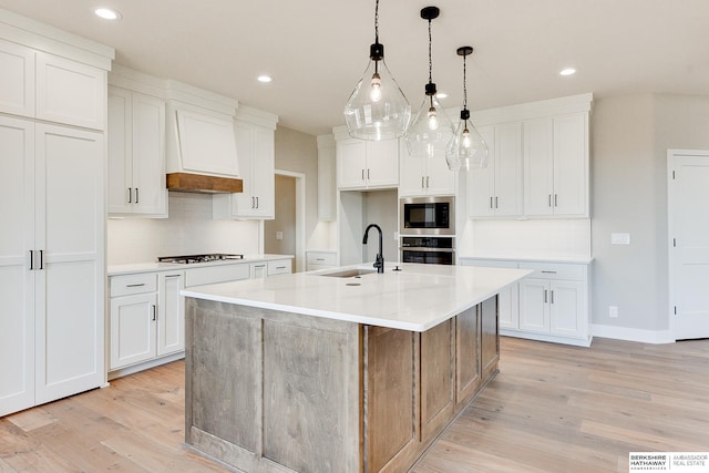 kitchen with built in microwave, sink, an island with sink, and white cabinets