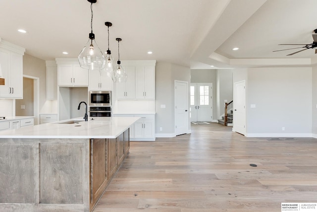 kitchen with built in microwave, sink, white cabinets, a large island with sink, and hanging light fixtures