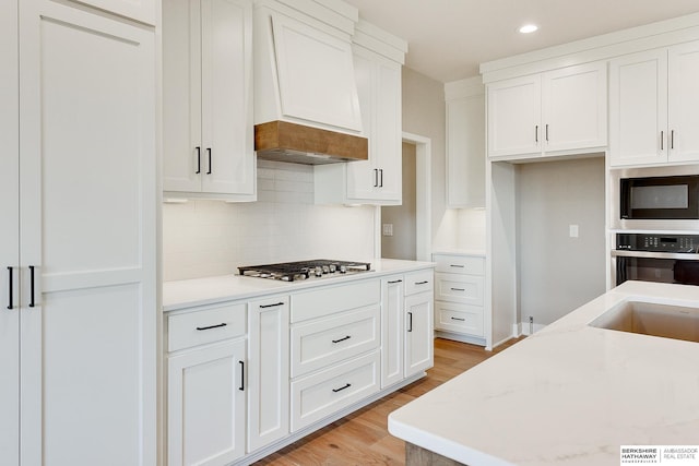 kitchen featuring light hardwood / wood-style flooring, appliances with stainless steel finishes, white cabinetry, light stone counters, and custom range hood