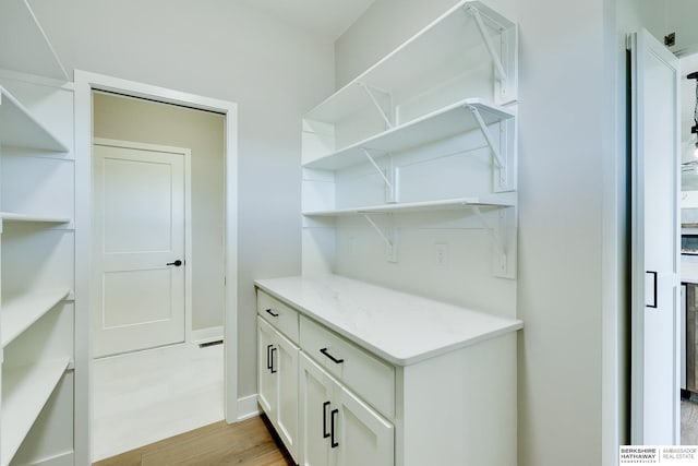 bar with white cabinetry, light stone counters, and light hardwood / wood-style flooring