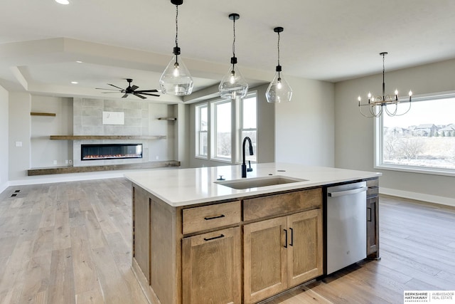 kitchen with sink, light hardwood / wood-style floors, a center island with sink, a tiled fireplace, and stainless steel dishwasher