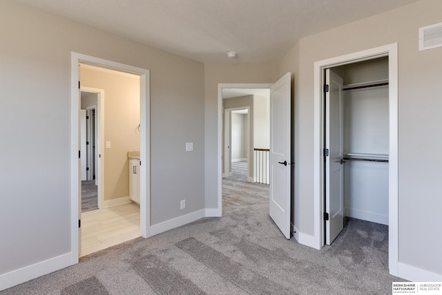 unfurnished bedroom with connected bathroom, light colored carpet, and a closet