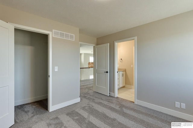 unfurnished bedroom with ensuite bath, light colored carpet, and a textured ceiling