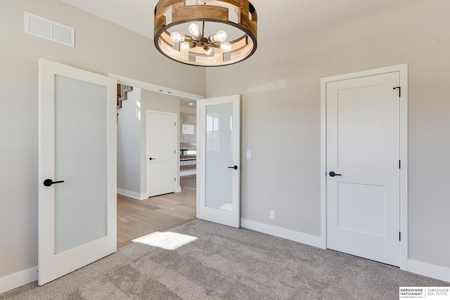 unfurnished bedroom featuring french doors, light colored carpet, and a notable chandelier