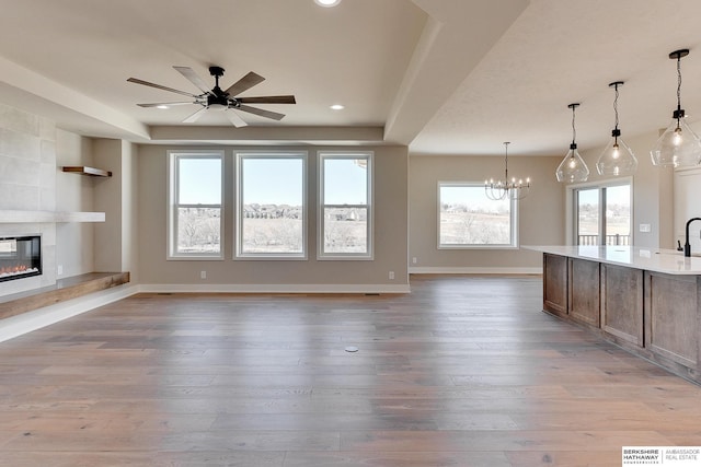 unfurnished living room featuring sink, ceiling fan with notable chandelier, a fireplace, and light hardwood / wood-style floors