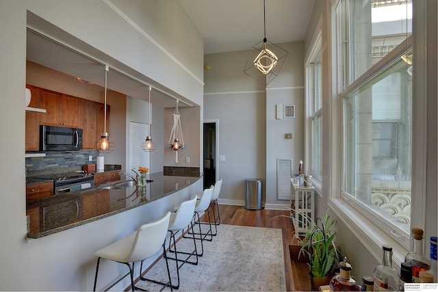 kitchen with wood-type flooring, backsplash, stainless steel range with electric stovetop, decorative light fixtures, and a breakfast bar