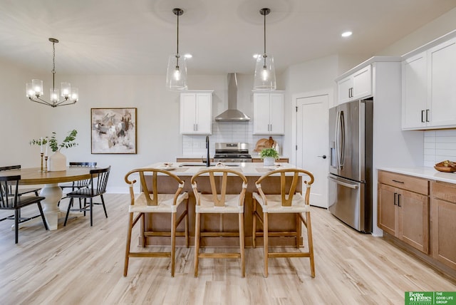 kitchen with appliances with stainless steel finishes, white cabinetry, wall chimney range hood, and light hardwood / wood-style floors