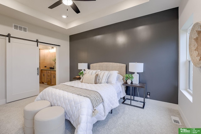 carpeted bedroom with a barn door, ceiling fan, a raised ceiling, and ensuite bath