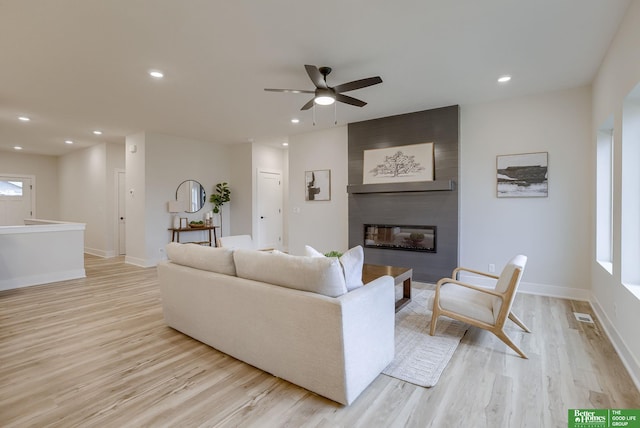 living room with a large fireplace, light hardwood / wood-style flooring, and ceiling fan