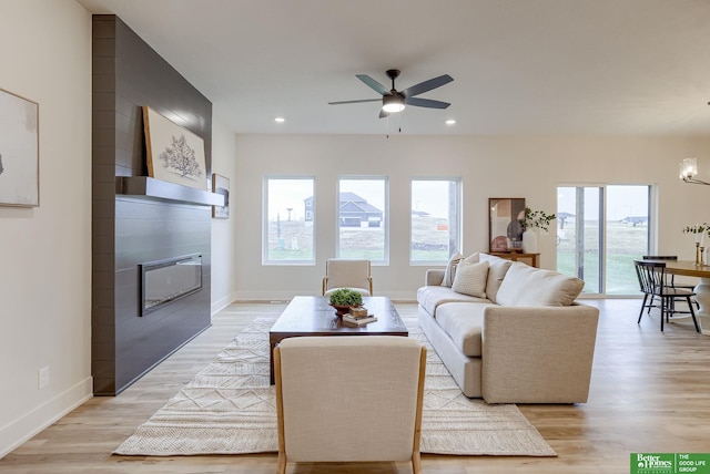 living room featuring a large fireplace, light wood-type flooring, and ceiling fan