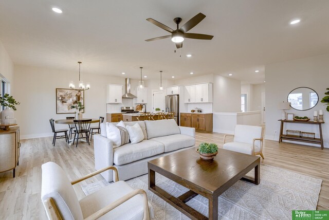 living room with light hardwood / wood-style floors, sink, and ceiling fan with notable chandelier