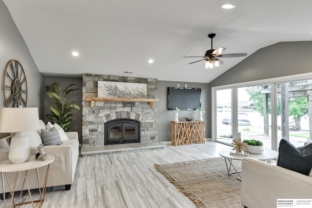 living room featuring light hardwood / wood-style floors, a stone fireplace, lofted ceiling, and ceiling fan