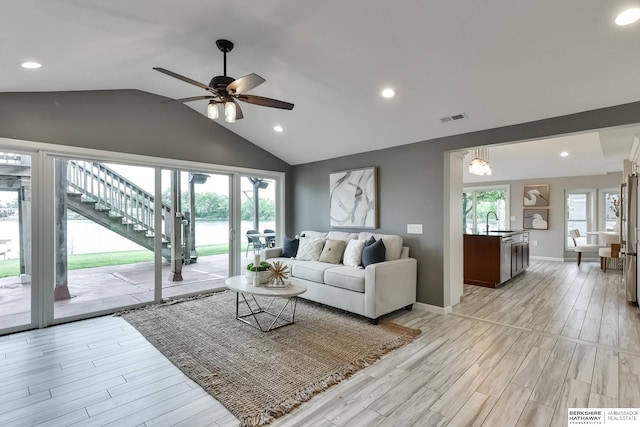 living room featuring light hardwood / wood-style flooring, lofted ceiling, sink, and a wealth of natural light