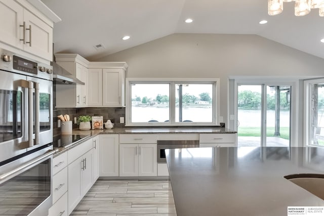 kitchen with black electric stovetop, wall chimney range hood, stainless steel double oven, white cabinets, and decorative backsplash