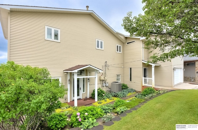 back of property with central AC unit, a garage, and a lawn