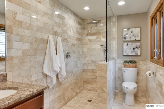 bathroom featuring tile patterned floors, toilet, vanity, tile walls, and a tile shower