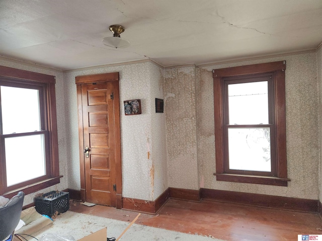 unfurnished room with wallpapered walls, plenty of natural light, light wood finished floors, and crown molding