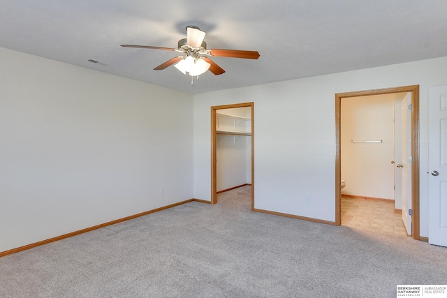 unfurnished bedroom featuring a closet, a walk in closet, light carpet, and ceiling fan