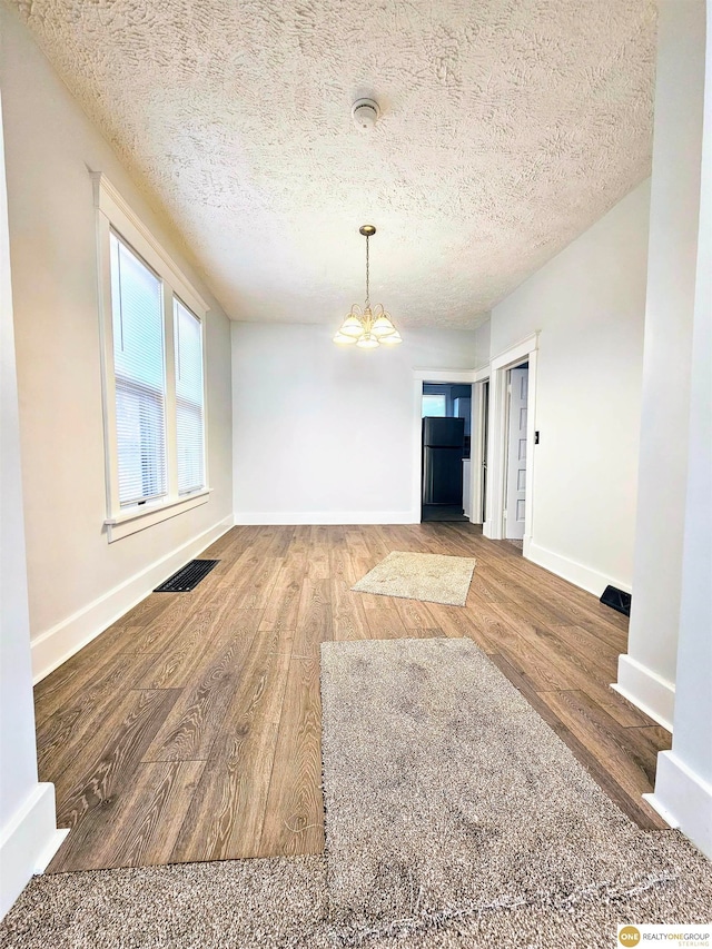 unfurnished dining area featuring a chandelier, wood-type flooring, and a textured ceiling