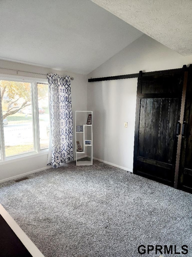 interior space with lofted ceiling, a textured ceiling, a barn door, and carpet floors