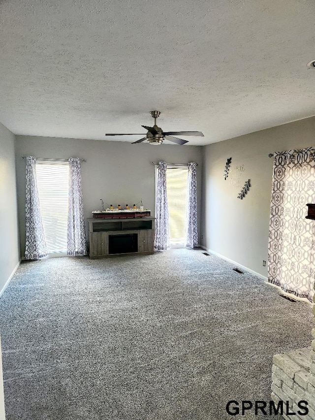 unfurnished living room featuring ceiling fan, carpet, and a textured ceiling