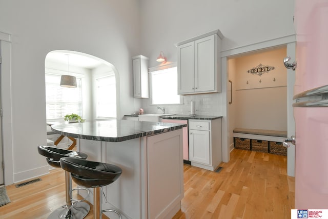 kitchen with a kitchen breakfast bar, hanging light fixtures, backsplash, white cabinets, and light hardwood / wood-style floors