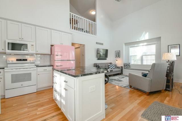 kitchen featuring white appliances, high vaulted ceiling, light wood-type flooring, and white cabinets