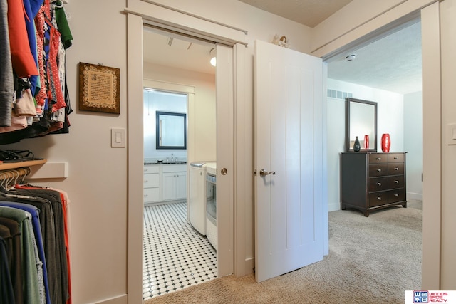 hall with light colored carpet, sink, and separate washer and dryer