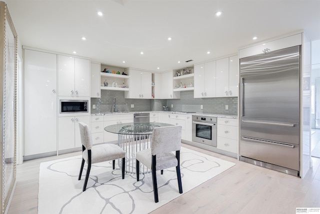 kitchen featuring built in appliances, sink, light wood-type flooring, and white cabinets