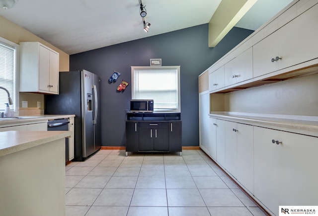 kitchen featuring lofted ceiling, light tile patterned floors, white cabinetry, rail lighting, and appliances with stainless steel finishes