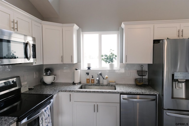 kitchen with tasteful backsplash, appliances with stainless steel finishes, white cabinetry, vaulted ceiling, and sink