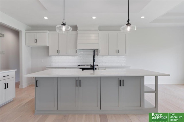 kitchen featuring backsplash, light hardwood / wood-style floors, decorative light fixtures, and a center island with sink