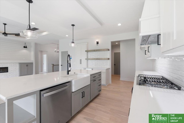 kitchen with stainless steel appliances, hanging light fixtures, sink, gray cabinets, and light wood-type flooring