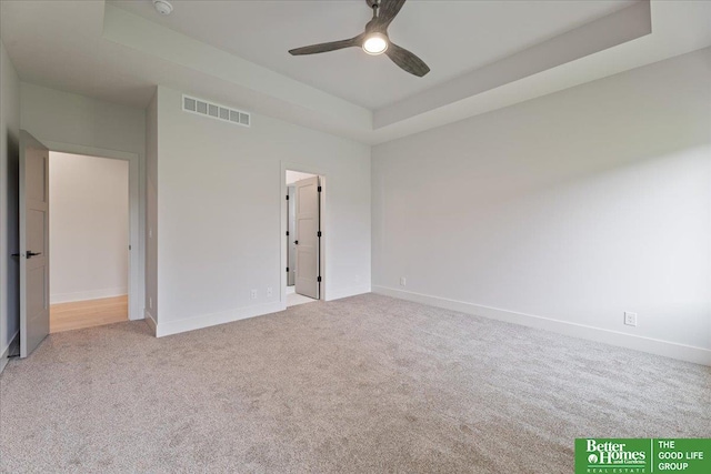 unfurnished bedroom featuring a tray ceiling, light colored carpet, and ceiling fan