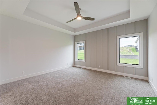 empty room with ceiling fan, carpet floors, and a tray ceiling