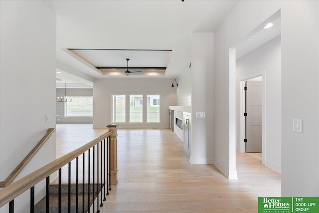 hall featuring light wood-type flooring, a notable chandelier, and a raised ceiling