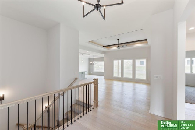 hallway featuring light hardwood / wood-style floors, a chandelier, a healthy amount of sunlight, and a tray ceiling