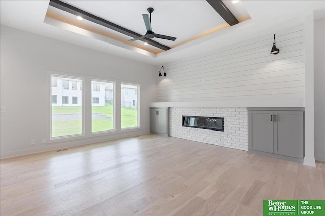 unfurnished living room with a fireplace, a tray ceiling, ceiling fan, and light hardwood / wood-style flooring