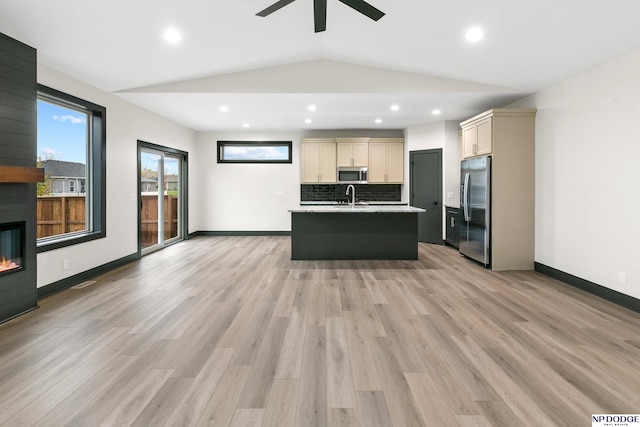 kitchen featuring appliances with stainless steel finishes, light hardwood / wood-style floors, a center island with sink, vaulted ceiling, and a large fireplace