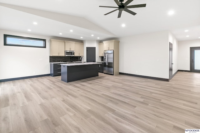 kitchen featuring light hardwood / wood-style floors, lofted ceiling, cream cabinets, an island with sink, and appliances with stainless steel finishes