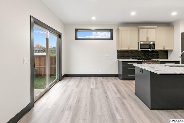 kitchen featuring sink, cream cabinets, appliances with stainless steel finishes, light wood-type flooring, and decorative backsplash