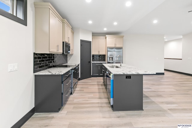 kitchen with a center island with sink, sink, light stone countertops, light wood-type flooring, and appliances with stainless steel finishes