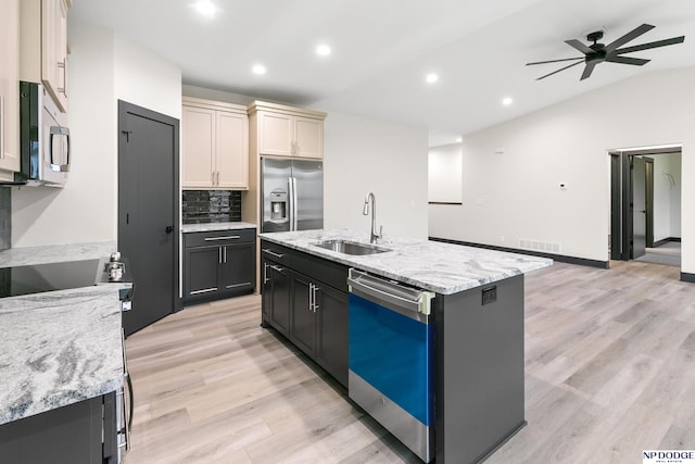 kitchen featuring sink, light stone counters, appliances with stainless steel finishes, an island with sink, and lofted ceiling